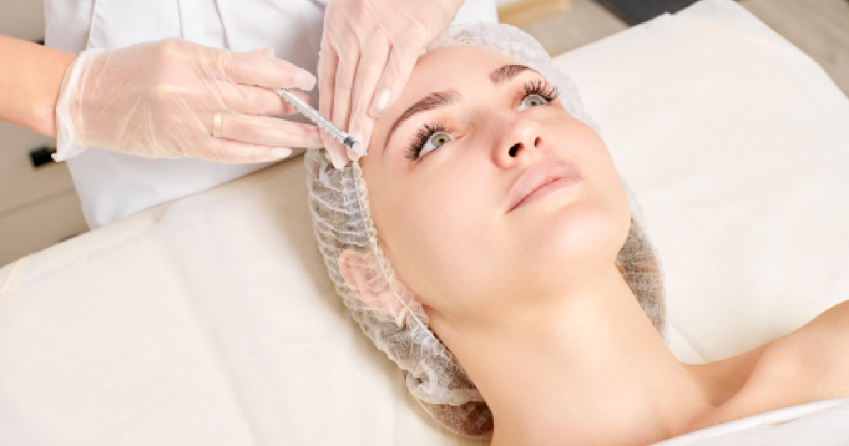 A woman receiving a forehead injection from a medical professional wearing gloves, illustrating a neuromodulator treatment in Oak Brook Terrace.